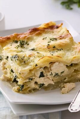 Close-up of a creamy white chicken spinach lasagna slice on a white plate with golden cheesy top