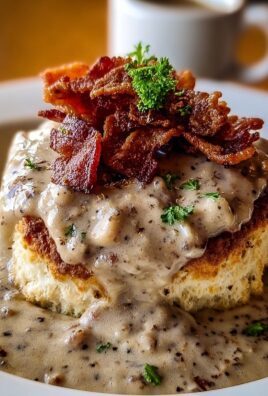Fluffy biscuit topped with creamy sausage gravy and crispy bacon pieces, garnished with fresh parsley