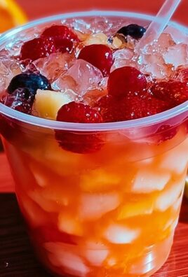 Vibrant fruit punch in a clear plastic cup with chopped fruit, ice cubes, and mixed berries