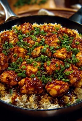 Sticky garlic chicken served over rice in a skillet and topped with fresh chopped green onions