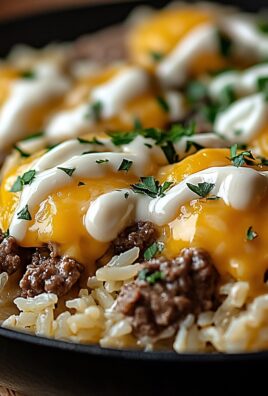 Close-up of beef and rice skillet topped with melted cheddar cheese, sour cream, and parsley in a black pan