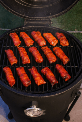 Golden bacon-wrapped bites sizzling on a charcoal grill with smoky heat rising in the background