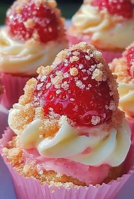 Close-up of strawberry shortcake cupcakes topped with cream cheese frosting, fresh strawberries, and crumbled topping