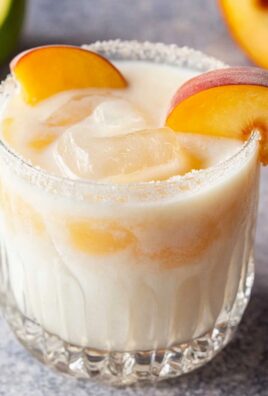 Chilled creamy peach cocktail with ice cubes and fresh peach slices in a sugar-rimmed glass