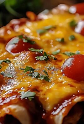 Close-up of cheesy enchiladas topped with melted cheddar, cherry tomatoes, and fresh cilantro