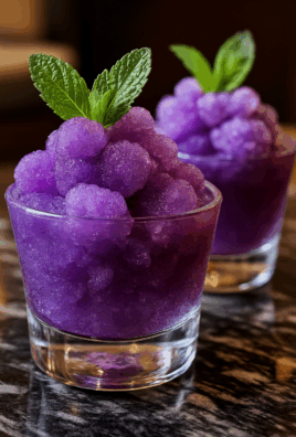 Close-up of vibrant purple grape granita in a clear glass, topped with a fresh mint sprig