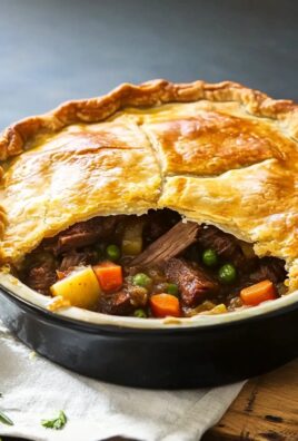 Golden beef pot pie with a flaky top crust cut open to reveal beef, carrots, peas, and potatoes