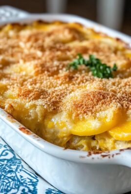 Baked yellow squash casserole in a white dish topped with golden buttery breadcrumbs and garnished with herbs