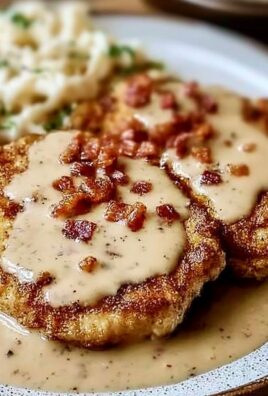 Crispy country fried pork chops topped with creamy bacon gravy and served with mashed potatoes