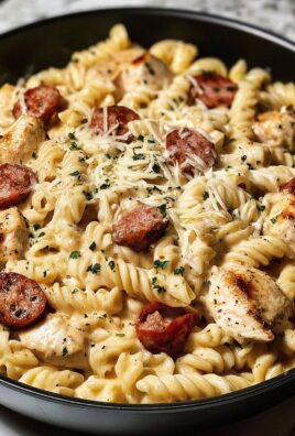 Skillet filled with creamy rotini pasta, grilled chicken, sausage slices, and shredded cheese