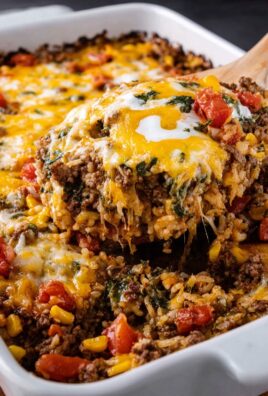Cheesy Mexican casserole with ground beef, rice, corn, tomatoes, and melted cheese being served from a white dish