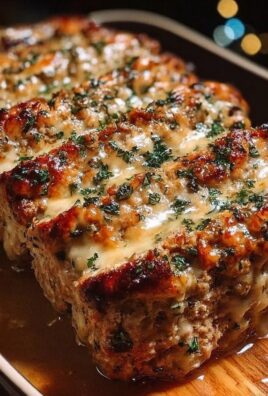 Garlic parmesan chicken meatloaf sliced in a pan, topped with melted cheese and parsley