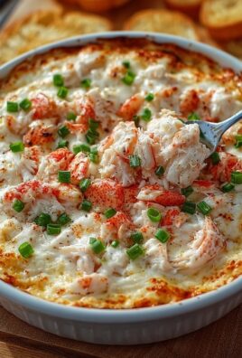 Hot cheesy crab dip topped with green onions in a white baking dish with a spoonful served